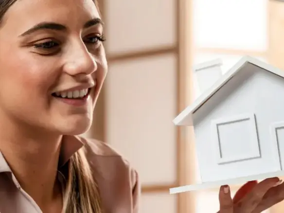 Mujer sonriente con un prototipo de casa en la mano.
